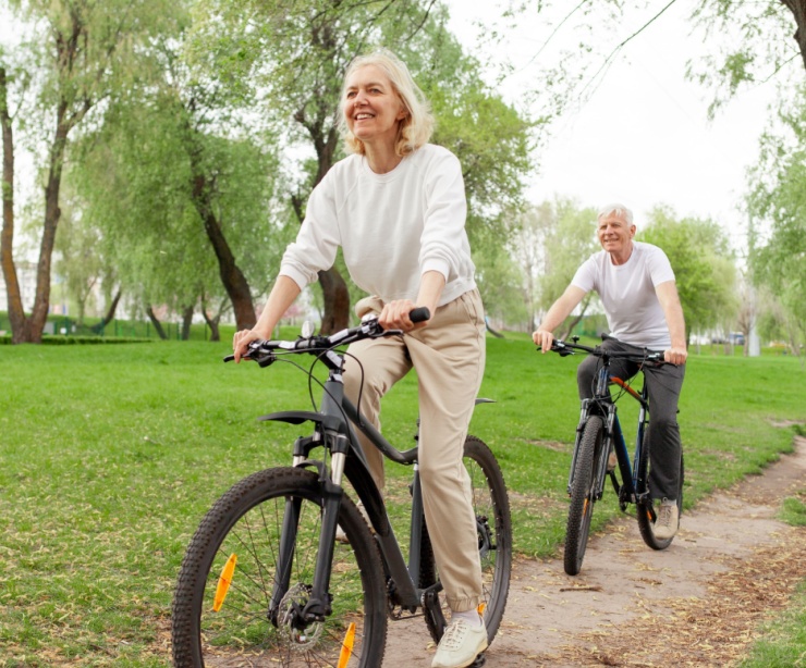 An elderly couple riding their bikes in the park.