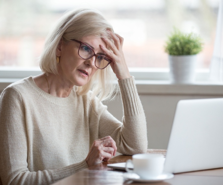A retired woman looking worried while using a laptop.
