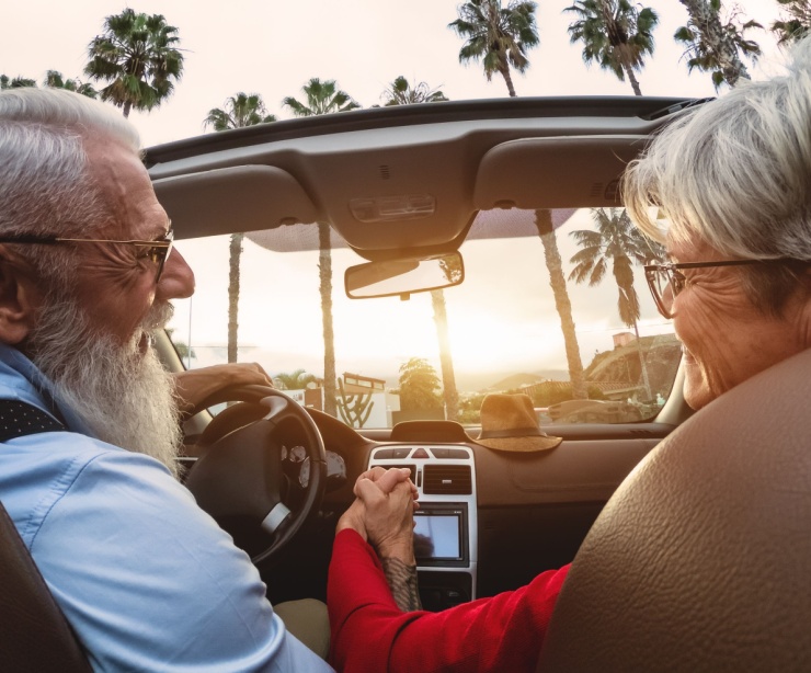 A happy older couple driving in a convertible car.