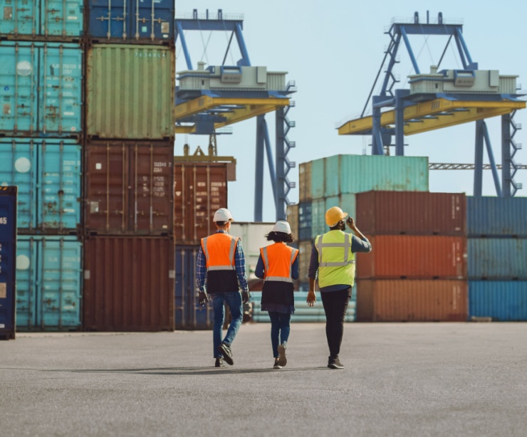 Workers walking through a shipping cargo container terminal depot.