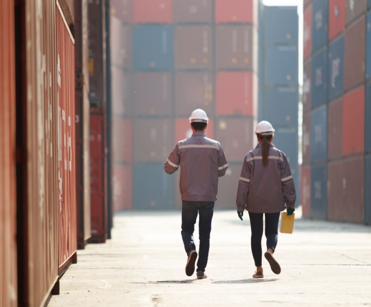 Two workers walking between shopping containers.