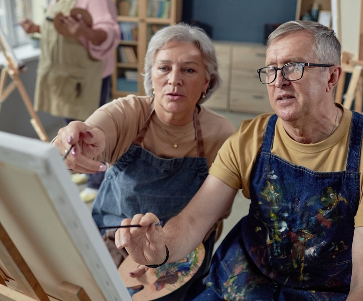 An older couple painting at an easel together.